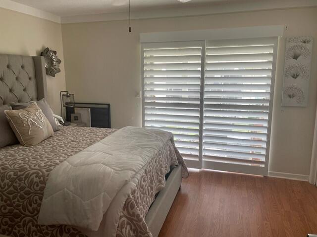 A bedroom features a tufted headboard, wood-look flooring, and white plantation shutters over sliding doors — 620 W Horizons W # 207, Boynton Beach FL 33435, BOYNTON BEACH, FL