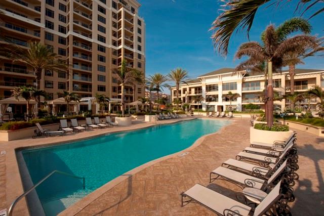 A swimming pool sits beside a large apartment building with lounge chairs on the deck — 11 BAYMONT STREET UNIT 504, CLEARWATER BEACH, FL