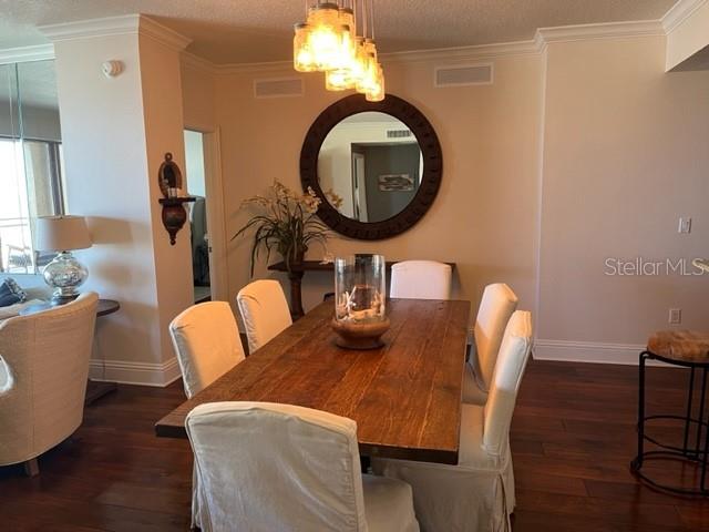 A dining room features a wooden table, upholstered chairs, a round mirror, and pendant lighting — 11 BAYMONT STREET UNIT 504, CLEARWATER BEACH, FL