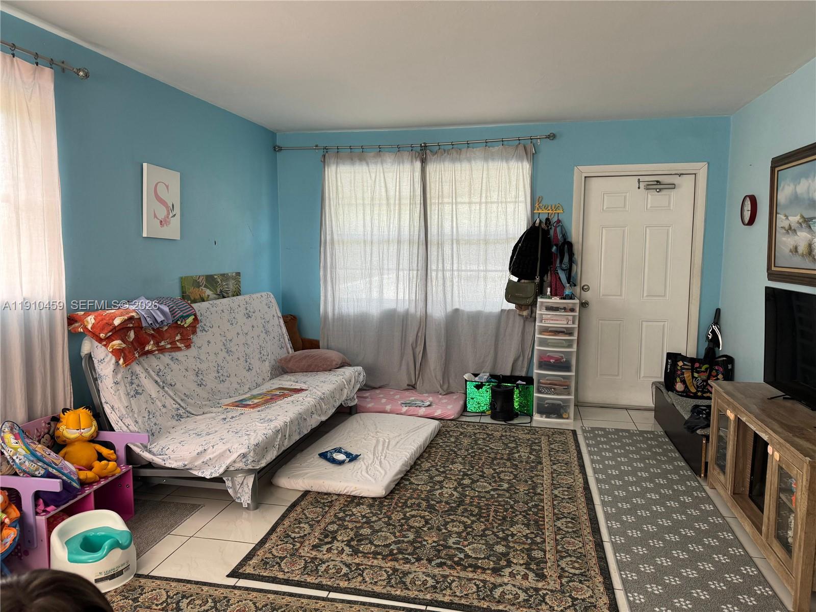 A living room with light blue walls, a futon, a rug, and a television console — 2444 Polk St # 210, Hollywood FL 33020, HOLLYWOOD, FL