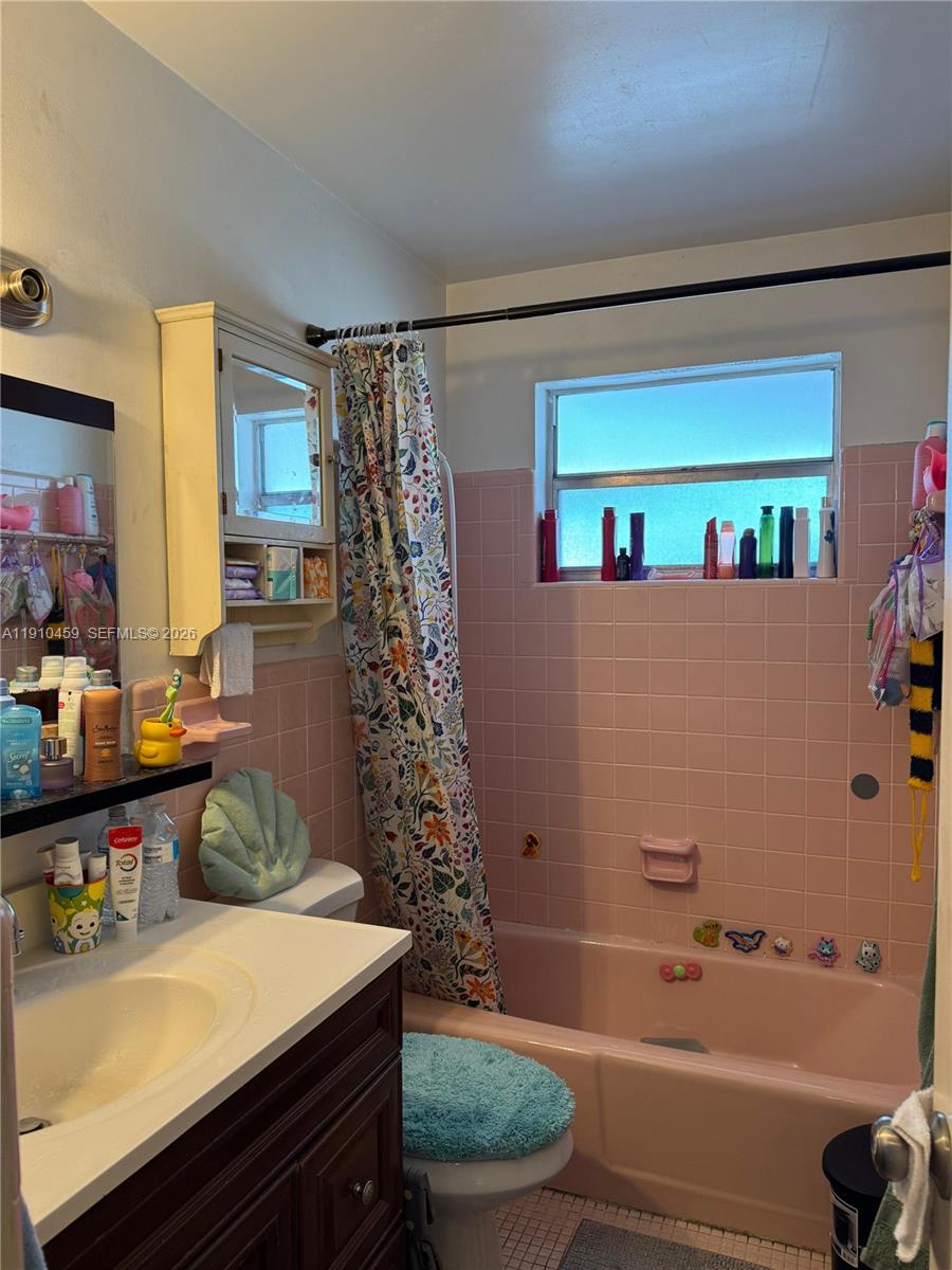 A bathroom features pink wall tiles, a matching pink bathtub, and a floral shower curtain — 2444 Polk St # 210, Hollywood FL 33020, HOLLYWOOD, FL