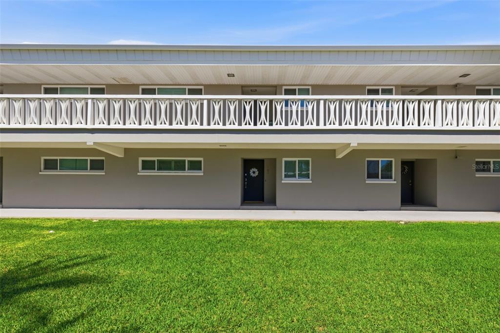A two-story apartment building exterior features a white balcony railing and a grassy lawn — 400 LARBOARD WAY UNIT 105, CLEARWATER BEACH, FL