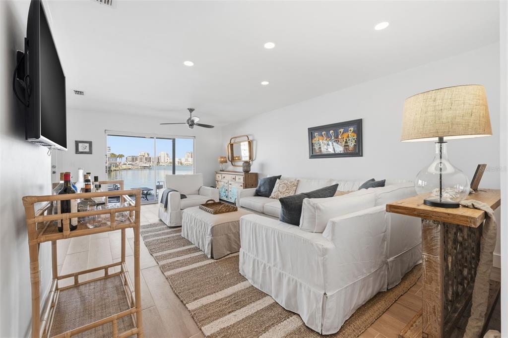 A bright living room features white slipcovered furniture, a rattan bar cart, and waterfront views — 400 LARBOARD WAY UNIT 105, CLEARWATER BEACH, FL