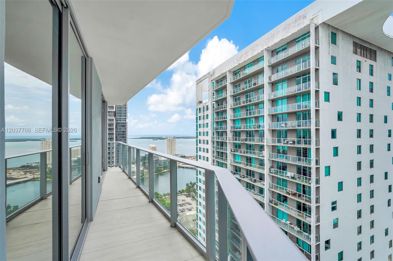 A high-rise balcony with a glass railing overlooks a bay and a neighboring apartment building — 77 SE 5th St # 3714, Miami FL 33131, MIAMI, FL
