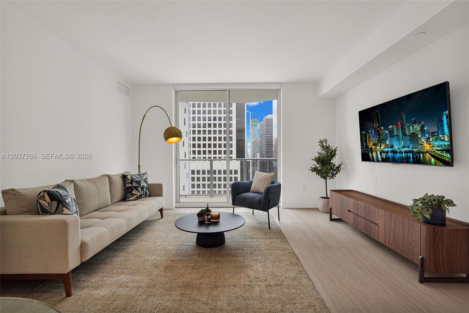 A modern living room features a beige sofa, dark armchair, media console, and city views — 77 SE 5th St # 3714, Miami FL 33131, MIAMI, FL