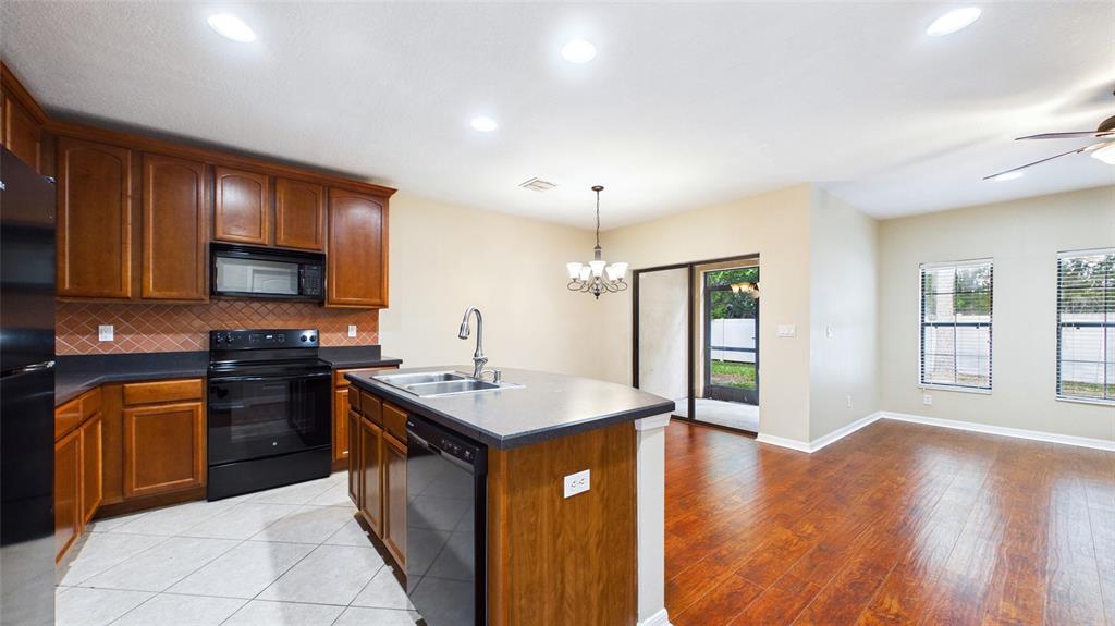 A kitchen with wood cabinets, a center island, and tile flooring opens to a dining area — 13128 LOGAN CAPTIVA LANE, GIBSONTON, FL