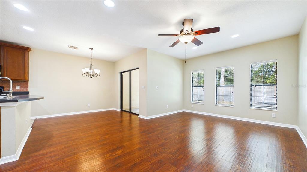 An open-concept dining and living area features wood-look flooring, a ceiling fan, and large windows — 13128 LOGAN CAPTIVA LANE, GIBSONTON, FL