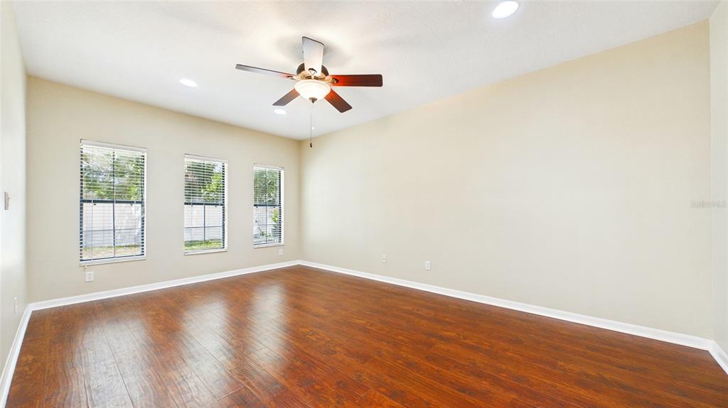 An empty room with wood-look flooring, three windows, and a ceiling fan — 13128 LOGAN CAPTIVA LANE, GIBSONTON, FL
