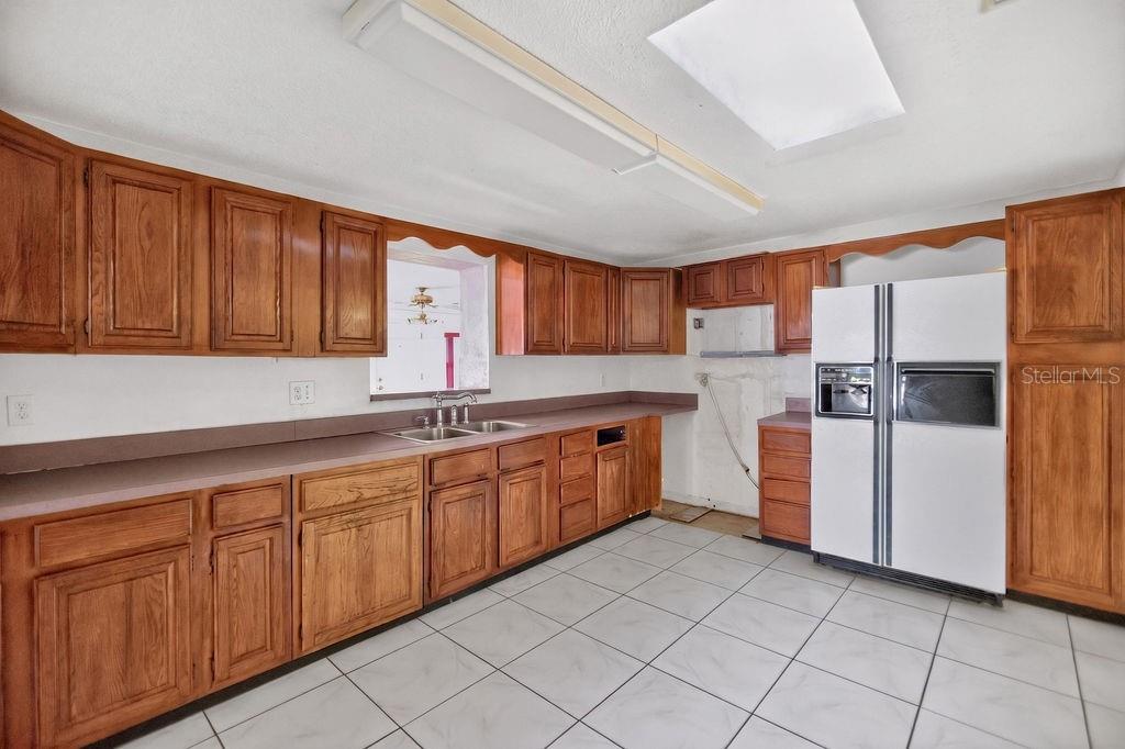 A kitchen features wood cabinets, white appliances, a double sink, and white tile flooring — 421 N FREDERICK AVENUE, DAYTONA BEACH, FL