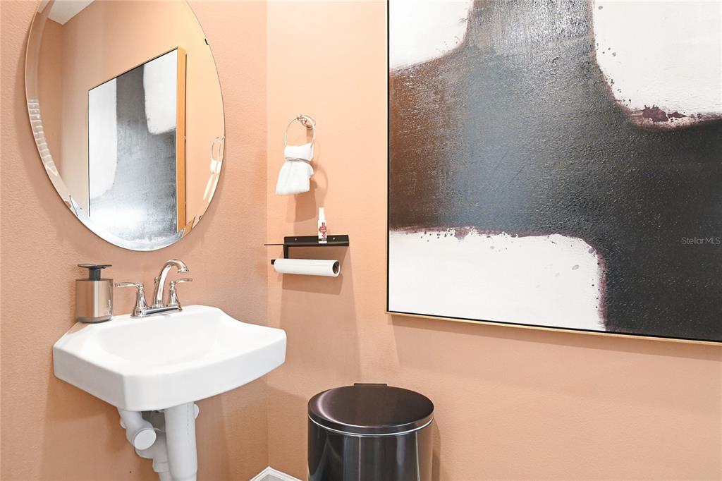A powder room features a wall-mounted sink, a round mirror, and abstract wall art — 2910 27TH AVENUE E, PALMETTO, FL