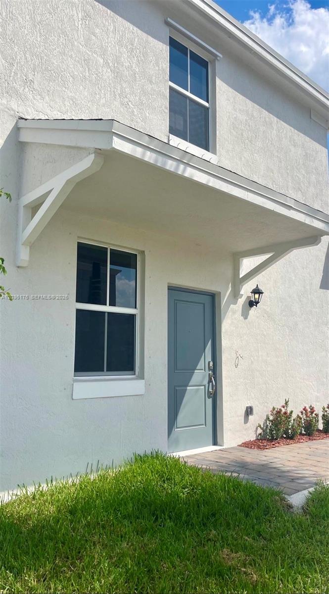 A white stucco exterior features a covered entryway, a gray door, and two windows — HOMESTEAD, FL