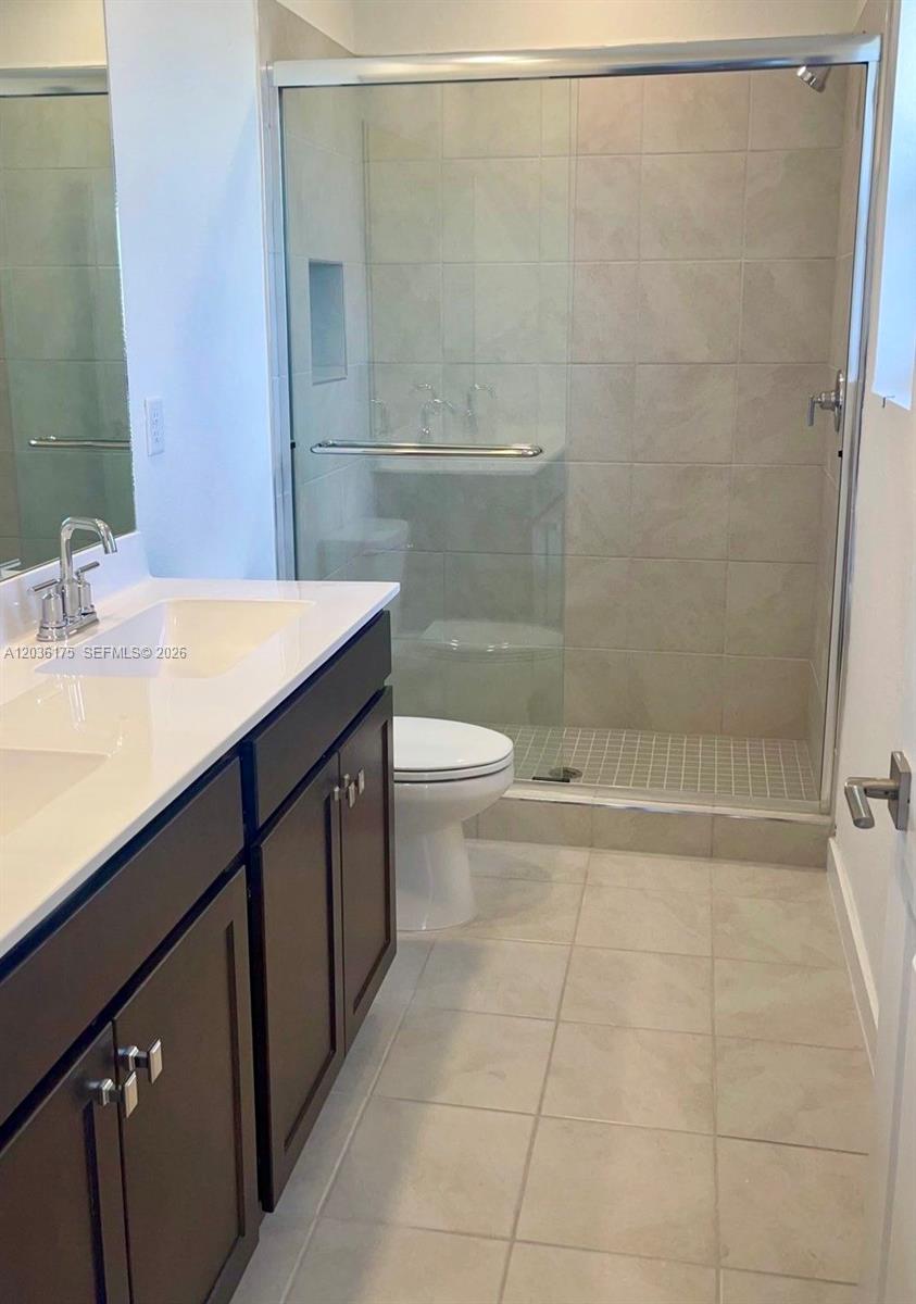 A bathroom features a double vanity with dark cabinets and a glass-enclosed walk-in shower — HOMESTEAD, FL