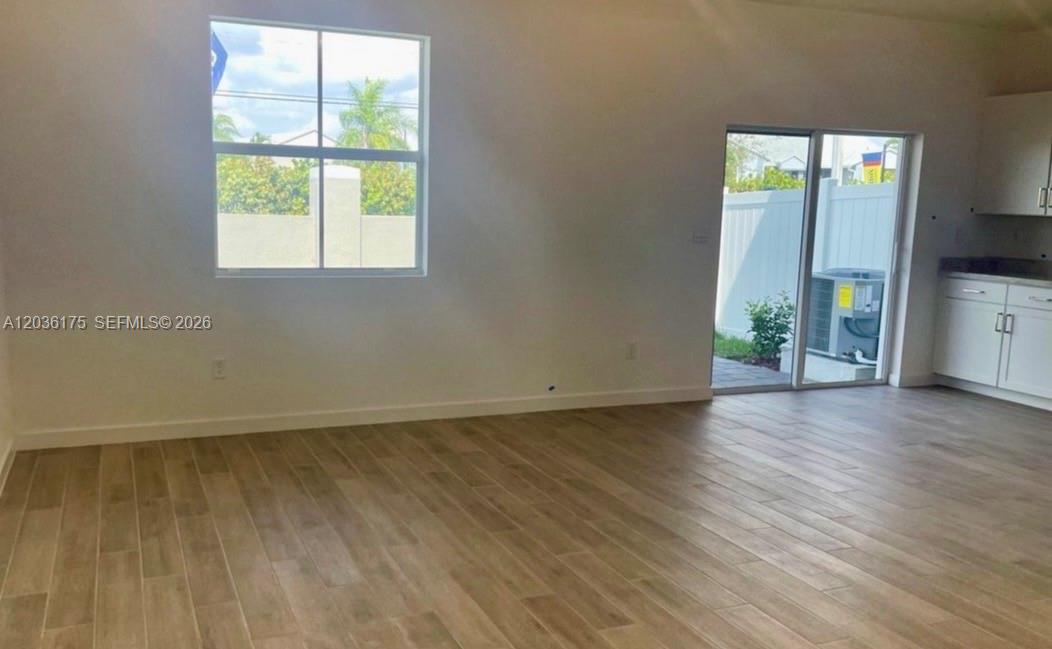 An open-concept room features light wood-look tile flooring, a window, and a sliding glass door — HOMESTEAD, FL