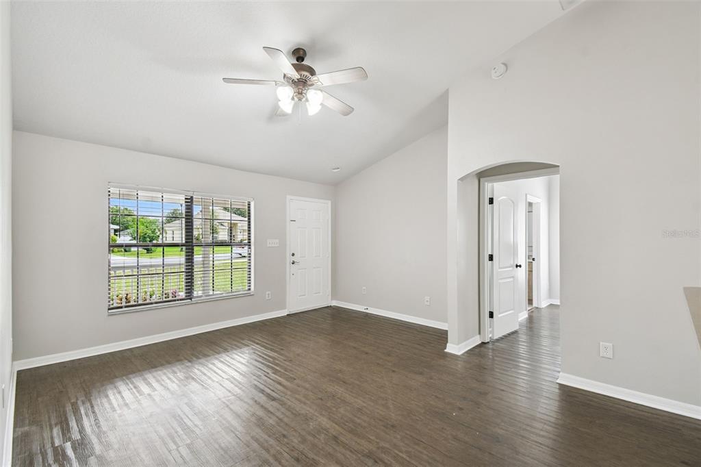 An empty living room features light gray walls, dark wood-look flooring, and a ceiling fan — 209 GOLDIE STREET, LEESBURG, FL