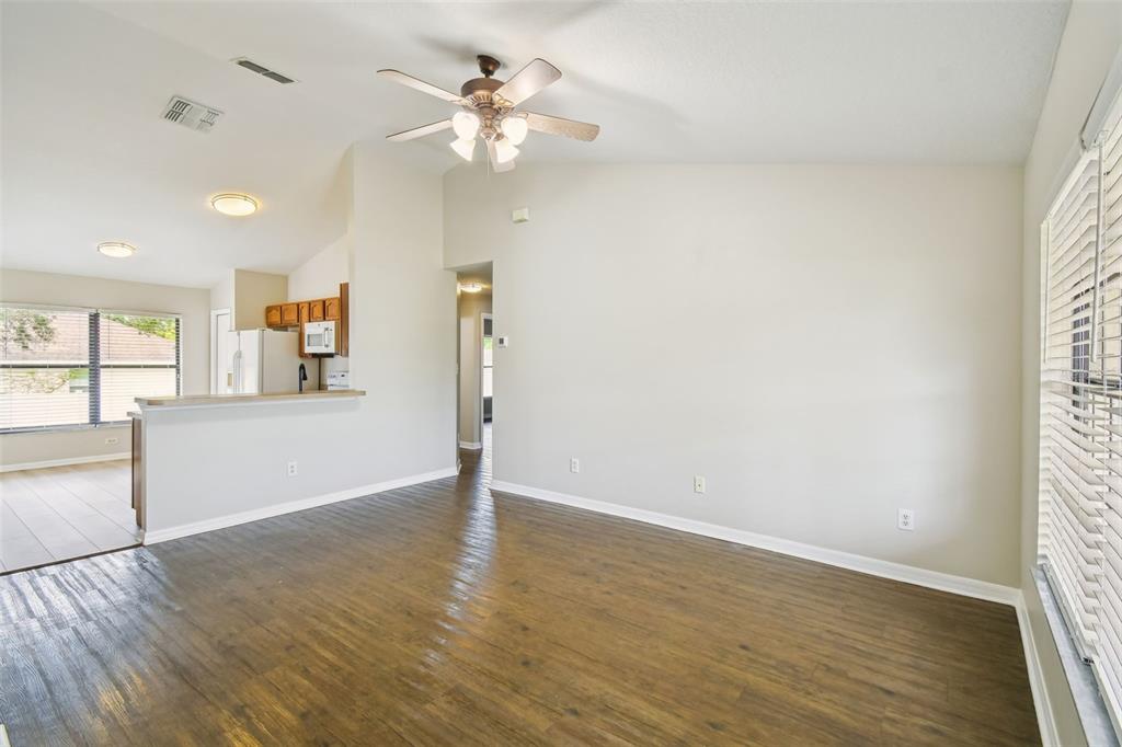 An empty living room with wood-look flooring, a ceiling fan, and an adjacent kitchen area — 209 GOLDIE STREET, LEESBURG, FL