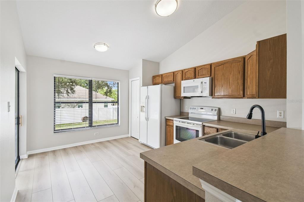 A kitchen with wood cabinets, white appliances, and a dining area with light wood flooring — 209 GOLDIE STREET, LEESBURG, FL