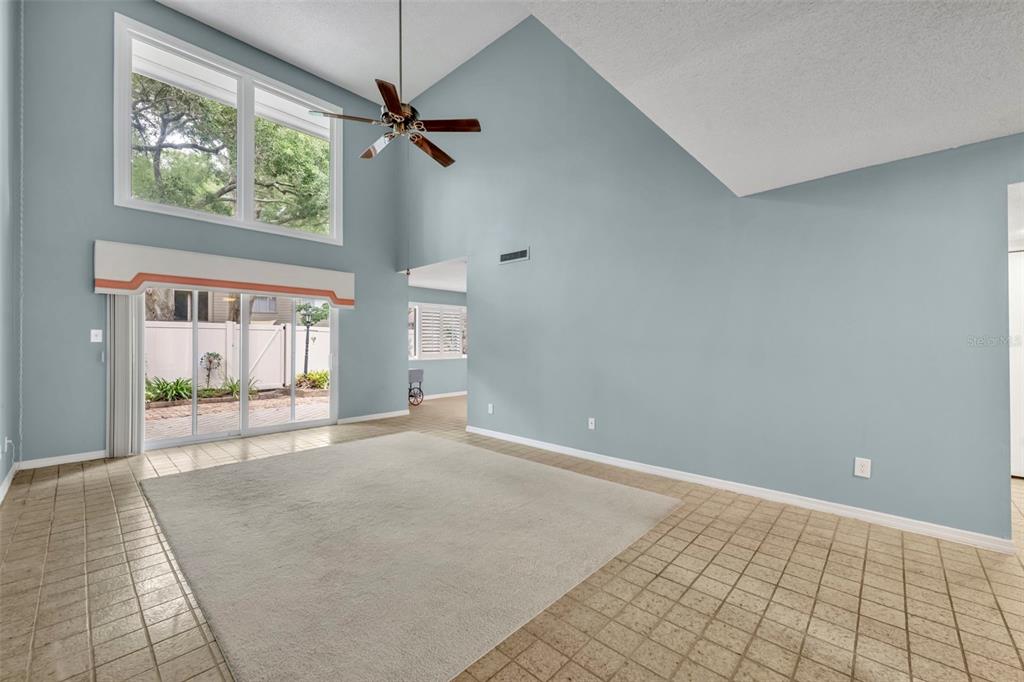 A living room with vaulted ceilings, light blue walls, tile flooring, and a sliding glass door — 497 OAK HAVEN DRIVE UNIT 497, ALTAMONTE SPRINGS, FL
