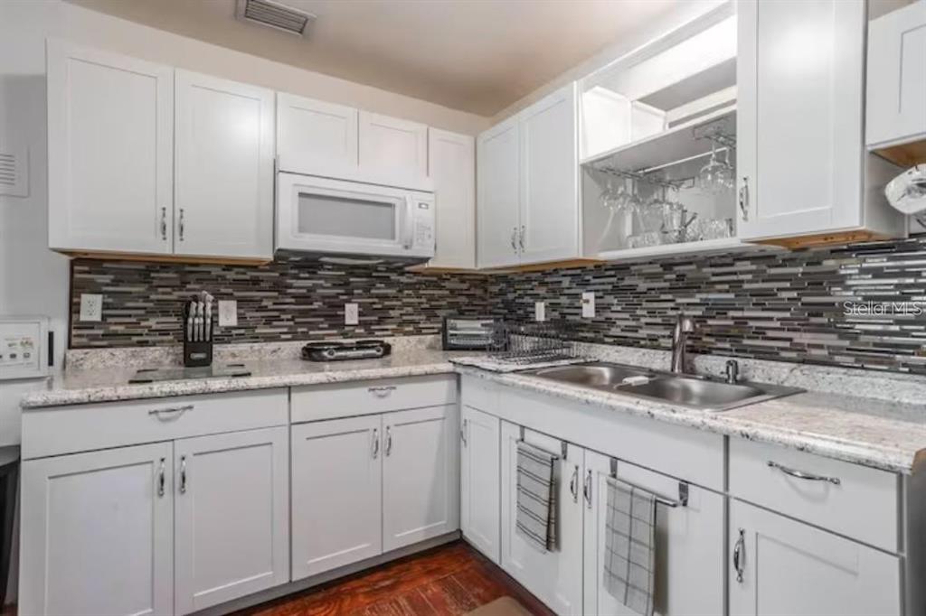 A kitchen features white cabinets, a mosaic tile backsplash, granite countertops, and a double sink — 3120 PEEL AVENUE, ORLANDO, FL