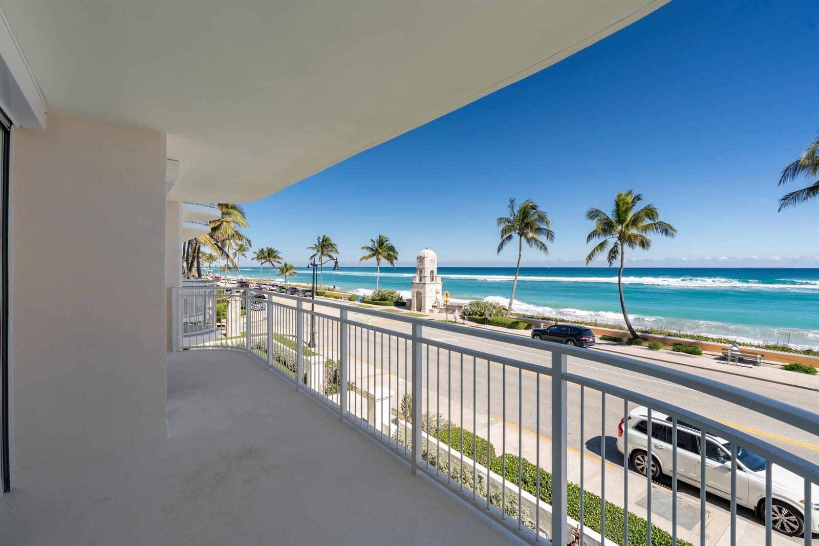 A balcony overlooks a coastal road, palm trees, a clock tower, and the ocean — 100 Worth Avenue # 310, Palm Beach FL 33480, PALM BEACH, FL