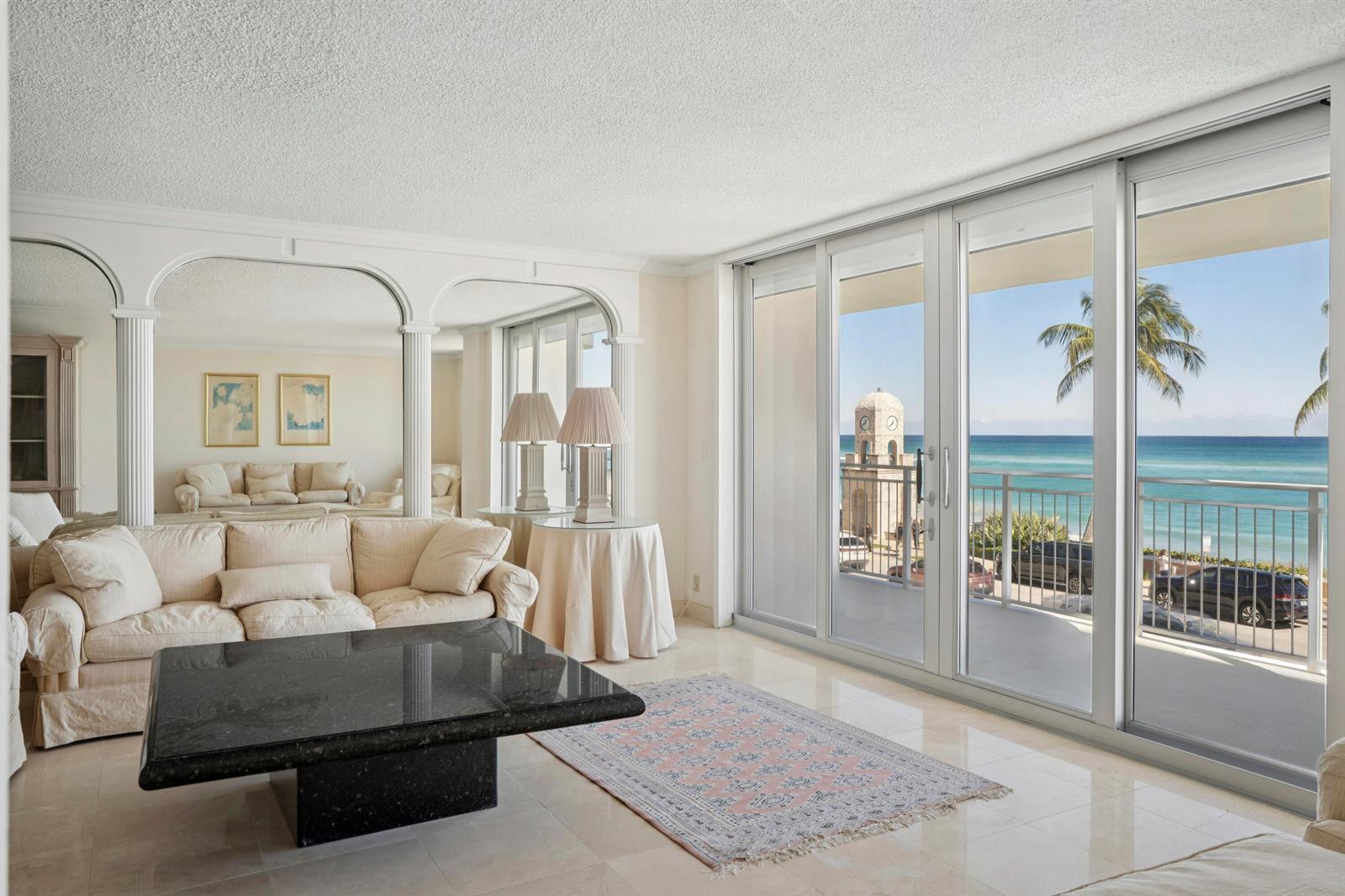 A living room with a black stone coffee table, beige sofa, and sliding doors overlooking the ocean — 100 Worth Avenue # 310, Palm Beach FL 33480, PALM BEACH, FL