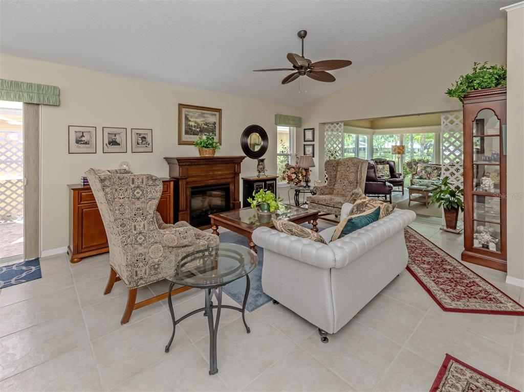 A living room features a fireplace, a patterned armchair, a white sofa, and tile flooring — 525 CLUBSIDE CIRCLE UNIT 53, VENICE, FL