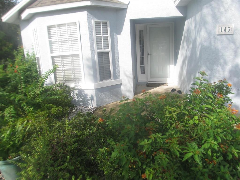 The exterior of a house features a white front door, a bay window, and landscaping — 145 CROOKED PINE ROAD, PORT ORANGE, FL