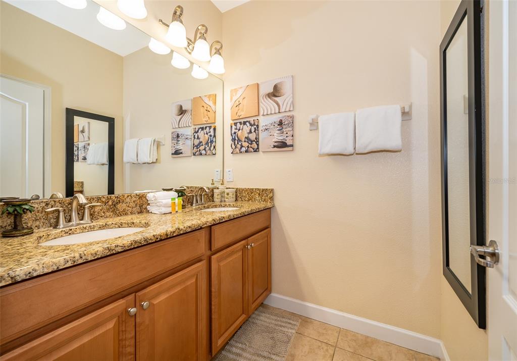 A bathroom features a double vanity with granite countertops, wood cabinets, and wall-mounted artwork — 8949 CANDY PALM ROAD, KISSIMMEE, FL