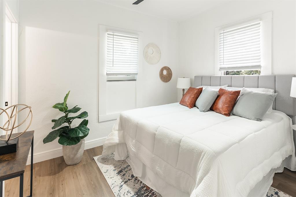 A bedroom features a bed with a gray headboard, white bedding, and wood-look flooring — 4324 EMERSON AVENUE S, ST PETERSBURG, FL