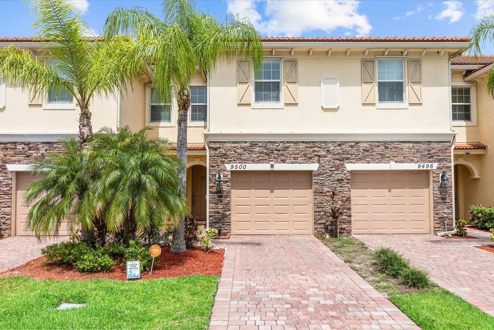 A two-story townhouse exterior features tan stucco walls, stone veneer, and two attached garages — 9500 SW Otter Lane, Stuart FL 34997, STUART, FL