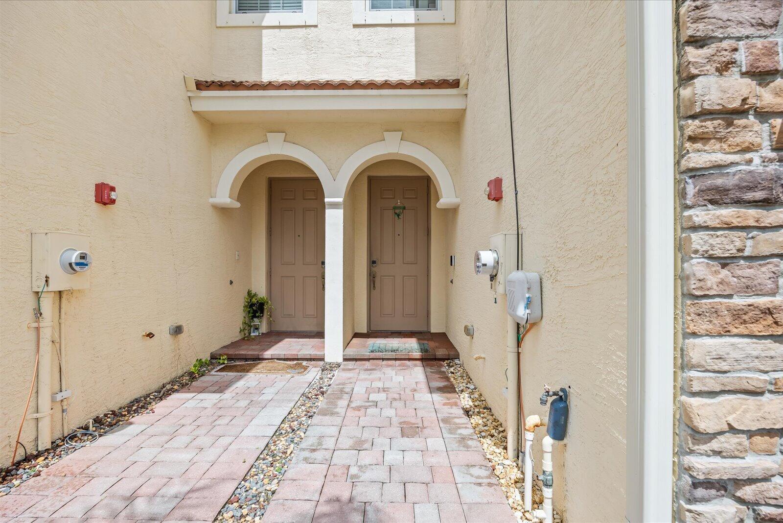 A paved walkway leads to two adjacent tan entry doors under a shared stucco archway — 9500 SW Otter Lane, Stuart FL 34997, STUART, FL