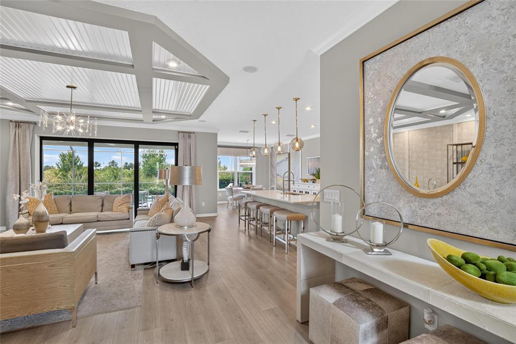 An open-concept living and kitchen area features a coffered ceiling, wood flooring, and gold accents — 8228 SUMMER NIGHT ROAD, SARASOTA, FL