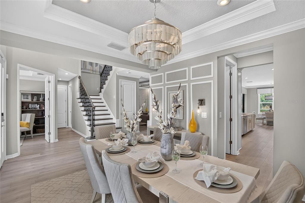 A dining room features a tiered chandelier, wainscoting, a wooden table, and light-colored flooring — 8228 SUMMER NIGHT ROAD, SARASOTA, FL