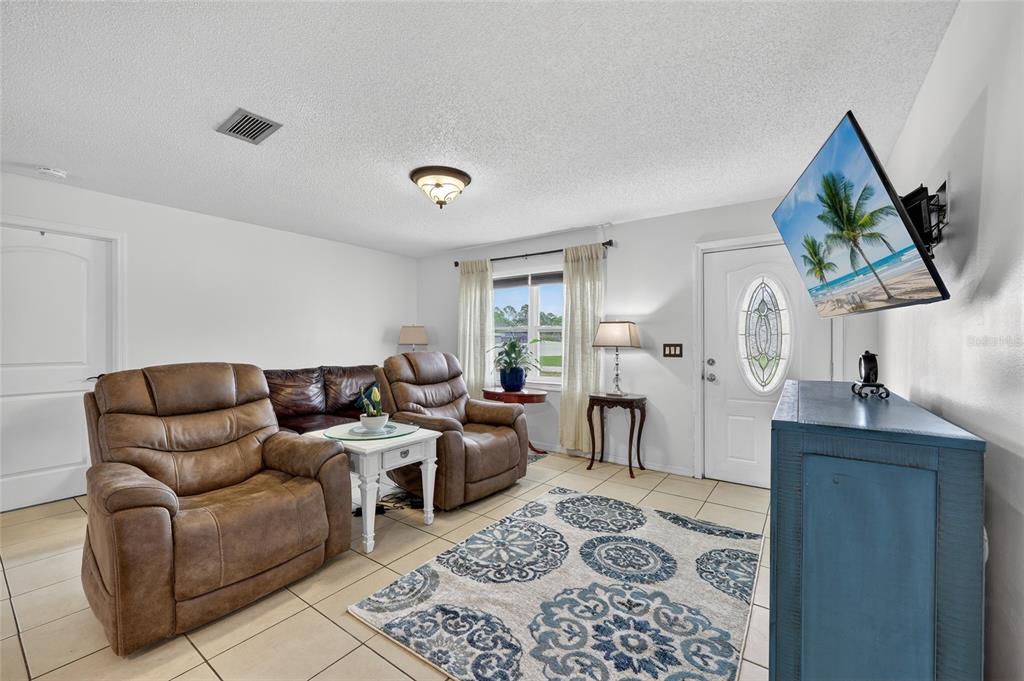 A living room features brown leather recliners, a patterned area rug, and a wall-mounted television — 27484 S TWIN LAKES DRIVE, PUNTA GORDA, FL