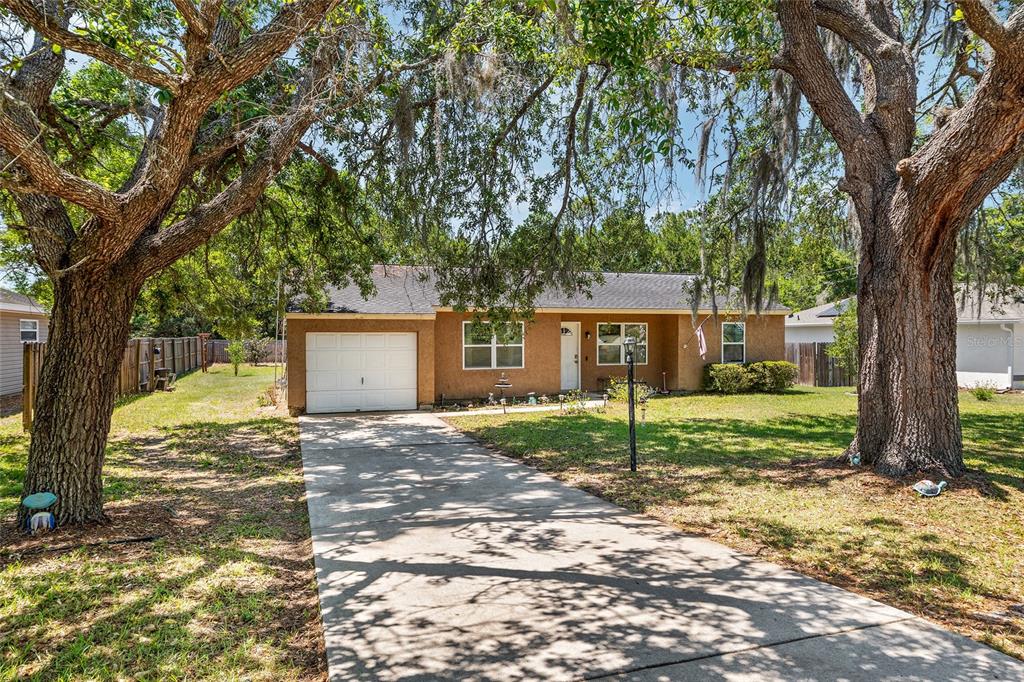 A single-story house with a tan exterior, a one-car garage, and large oak trees — 18 OLIVE CIRCLE, OCALA, FL