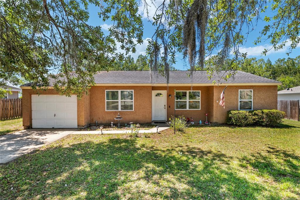 A single-story house with a tan stucco exterior, a white garage door, and a front lawn — 18 OLIVE CIRCLE, OCALA, FL