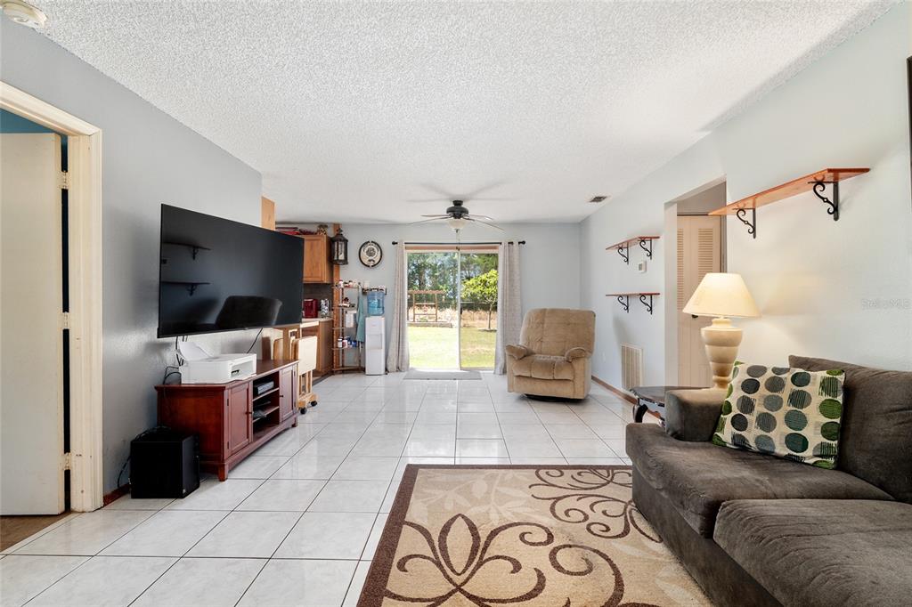 A living room with white tile floors, a television, a recliner, and a sliding glass door — 18 OLIVE CIRCLE, OCALA, FL