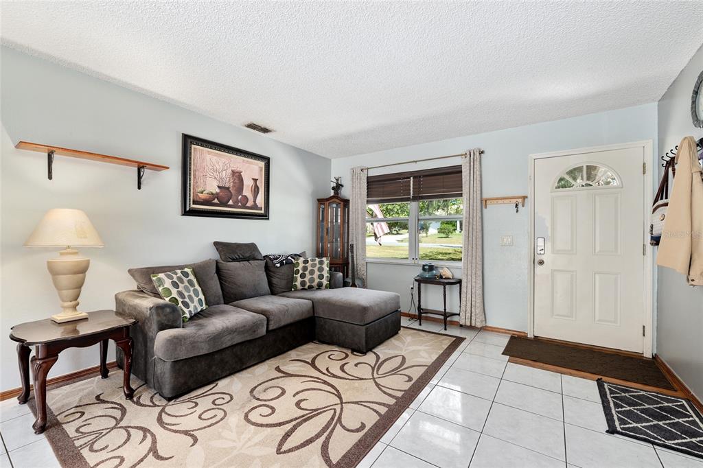 A living room features a gray sectional sofa, a patterned area rug, and white tile flooring — 18 OLIVE CIRCLE, OCALA, FL
