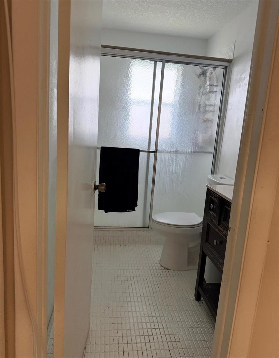 A bathroom features a tiled floor, a toilet, a dark vanity, and a glass shower enclosure — 5515 Lakewood Circle # 125, Pompano Beach FL 33063, POMPANO BEACH, FL