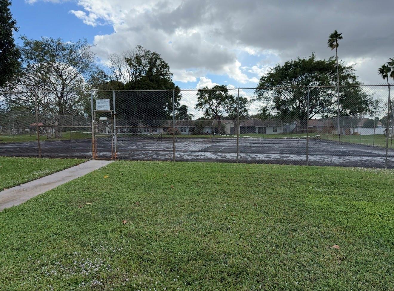 A fenced-in tennis court with a paved walkway in a grassy outdoor area — 5515 Lakewood Circle # 125, Pompano Beach FL 33063, POMPANO BEACH, FL