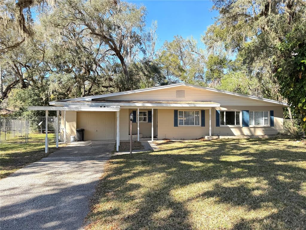 A single-story house with a carport, tan siding, and blue shutters sits on a grassy lot — 310 LONGWOOD DRIVE, BROOKSVILLE, FL