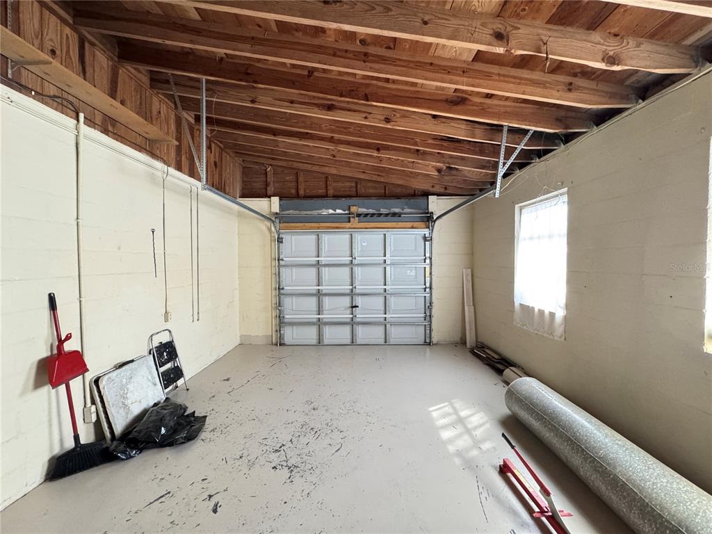 An unfinished garage features concrete block walls, a sloped wooden ceiling, and a roll-up door — 310 LONGWOOD DRIVE, BROOKSVILLE, FL