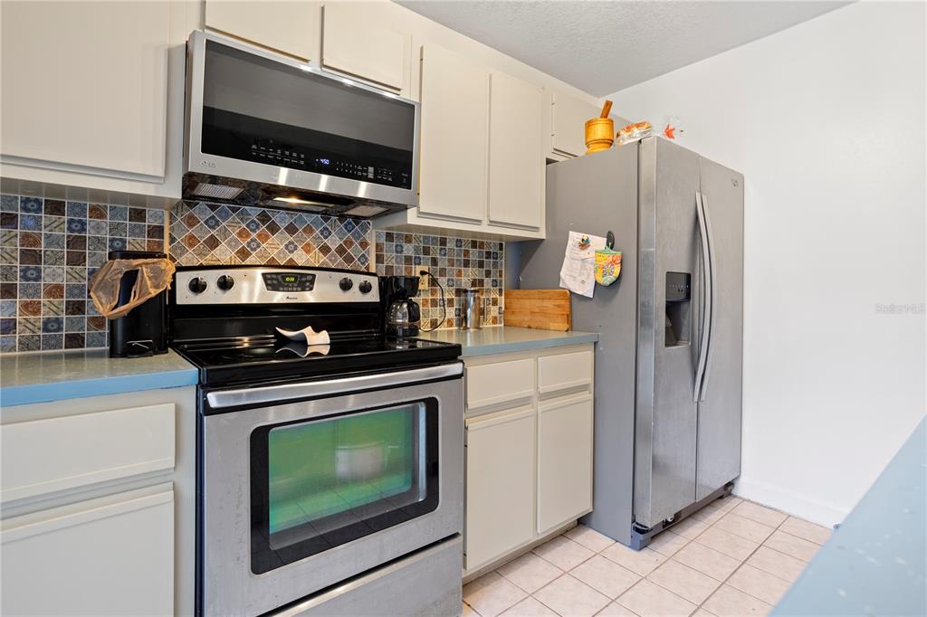 A kitchen features stainless steel appliances, light-colored cabinets, and a multi-colored mosaic tile backsplash — 5284 WILLOW COURT UNIT 508, ORLANDO, FL