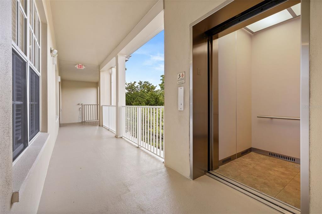 An open-air hallway features a metal elevator, white railings, and an exit sign — 855 BLUE SAGE STREET UNIT 302, CELEBRATION, FL