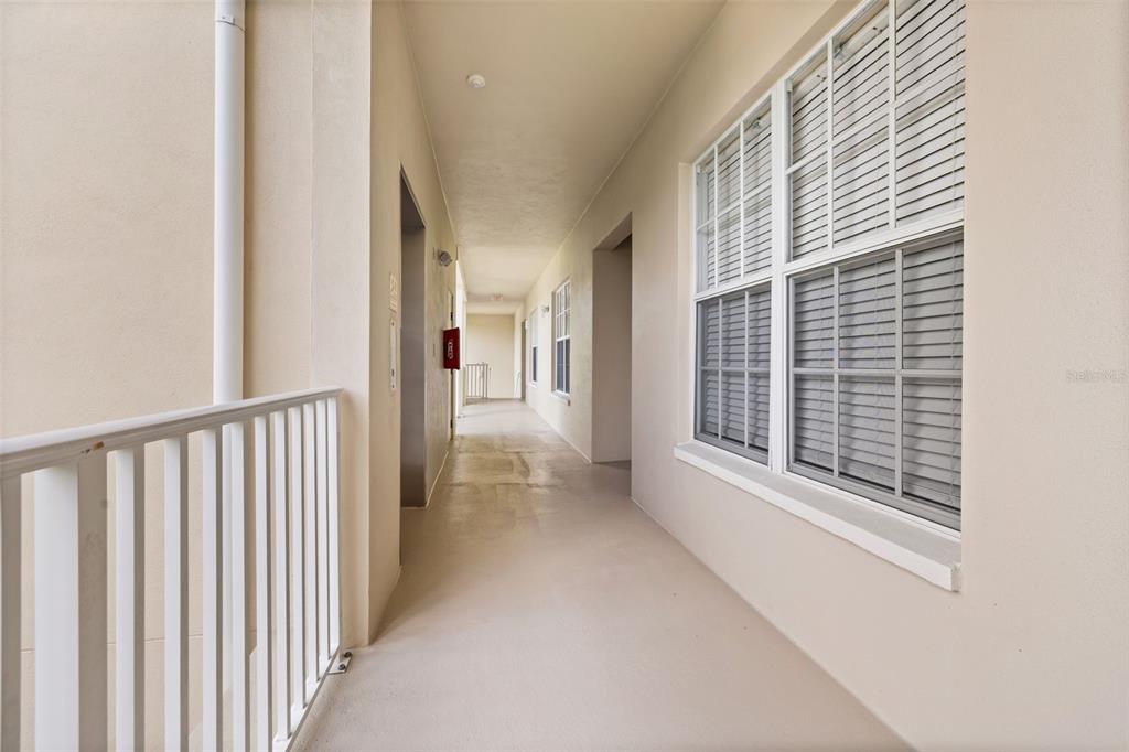 An outdoor apartment hallway with a white railing, beige walls, and a window with blinds — 855 BLUE SAGE STREET UNIT 302, CELEBRATION, FL