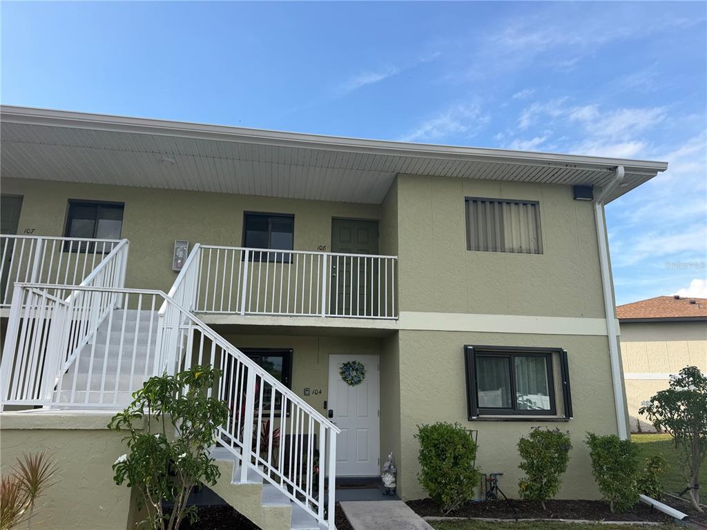 A two-story apartment building exterior features a white staircase leading to an upper balcony — 25225 RAMPART BOULEVARD UNIT 108, PUNTA GORDA, FL