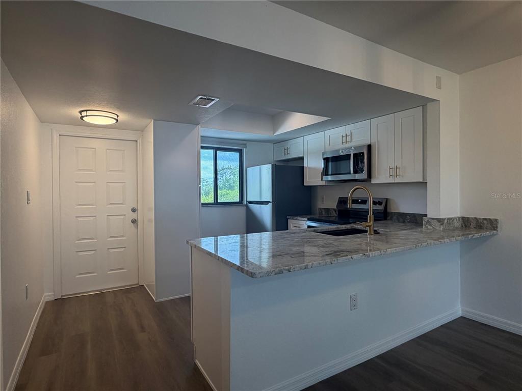 A kitchen with white cabinets, granite countertops, and a breakfast bar overlooks a living area — 25225 RAMPART BOULEVARD UNIT 108, PUNTA GORDA, FL
