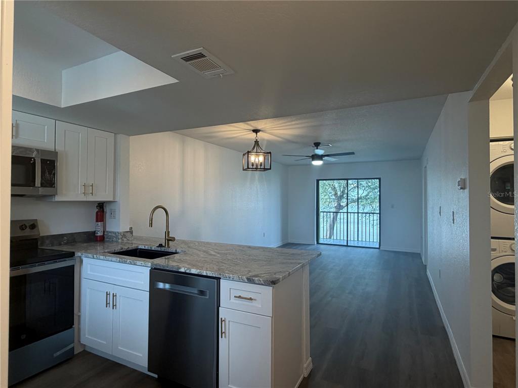 A kitchen with white cabinets and granite countertops opens to a living area with balcony access — 25225 RAMPART BOULEVARD UNIT 108, PUNTA GORDA, FL