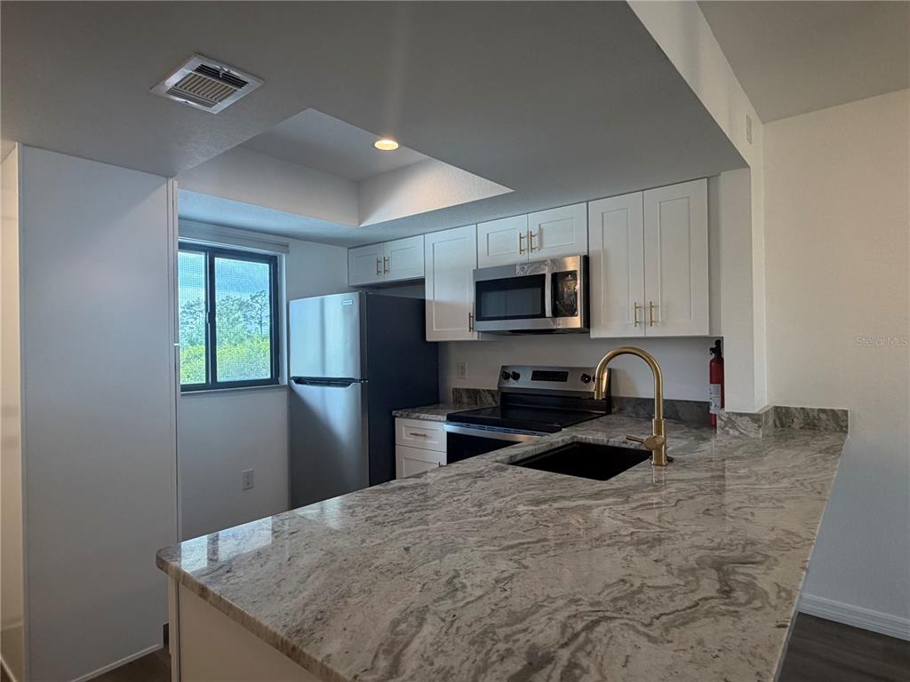 A kitchen features white cabinets, stainless steel appliances, and a granite countertop with a sink — 25225 RAMPART BOULEVARD UNIT 108, PUNTA GORDA, FL