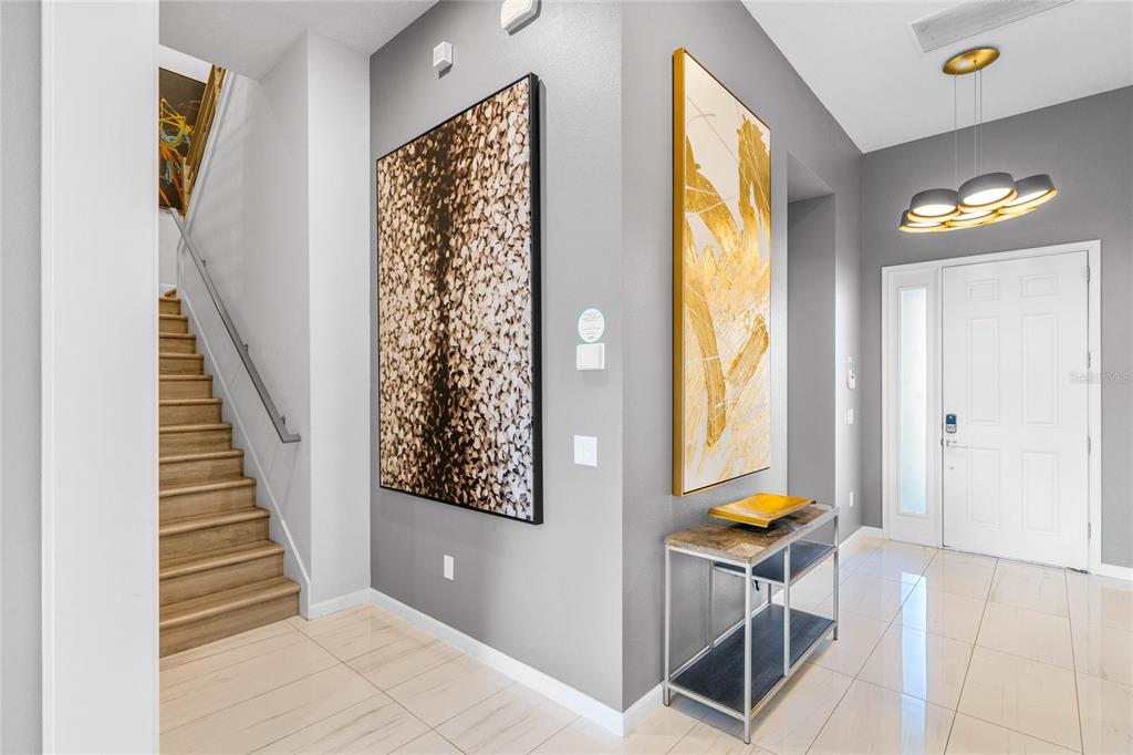 A modern entryway features a staircase, two large wall paintings, and a console table — 1743 OAK BLOSSOM DRIVE, DAVENPORT, FL