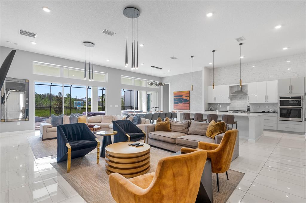 A spacious open-concept living room and kitchen featuring modern furniture, tile floors, and large windows — 1743 OAK BLOSSOM DRIVE, DAVENPORT, FL